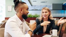 Two people sitting at a table while talking and looking at a computer