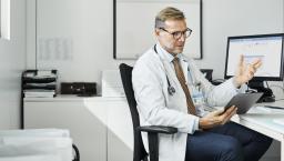 Doctor sitting in a chair at a desk while looking at a tablet