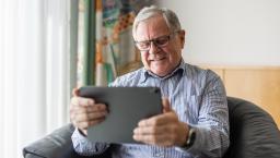 Person sitting in a chair in a home smiling while looking at a tablet