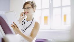 Healthcare provider sitting in an office wearing a stethoscope and looking at a tablet