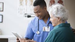 Healthcare provider standing in a clinic next to a patient while looking at a tablet