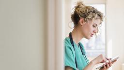 Nurse standing in a hallway while looking at a tablet