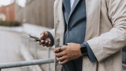 Midsection of a person in a suite wearing two rings and looking at their phone