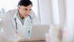 Healthcare provider wearing a lab coat with a stethoscope around their neck while looking at a computer