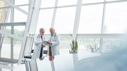 Two healthcare professionals standing in a large room with windows