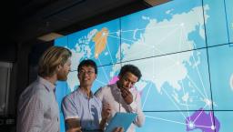 Three people standing in front of a large board showing the world map