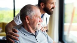 Person sitting in a chair while looking out a window with another person standing beside them