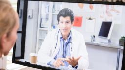 Healthcare provider on a computer screen talking to someone sitting at a desk