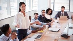 Several people sitting in a board room looking at one person standing up