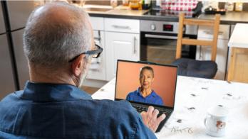 Person sitting at a table while looking at a computer with a person on it