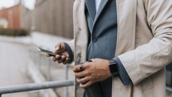 Midsection of a person in a suite wearing two rings and looking at their phone