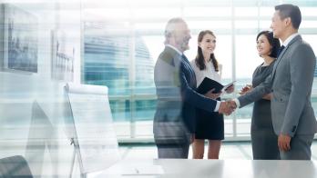 Two people standing in a room shaking hands while two other people stand by them and watch