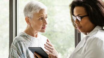 Healthcare provider standing next to a patient while looking at a tablet