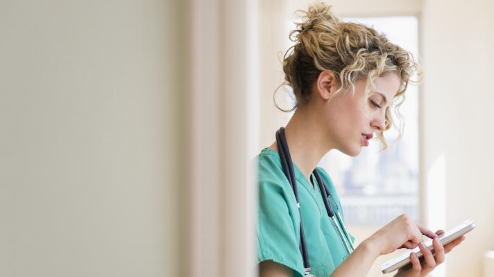 Nurse standing in a hallway while looking at a tablet