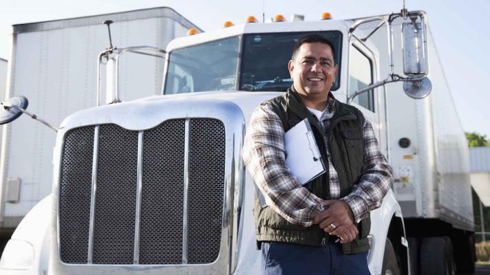 Truck driver standing in front of a semi-truck while holding a clipboard