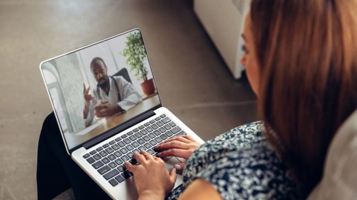 Person sitting on their couch with a computer on their lap talking to a virtual healthcare provider