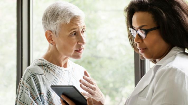 Healthcare provider standing next to a patient while looking at a tablet